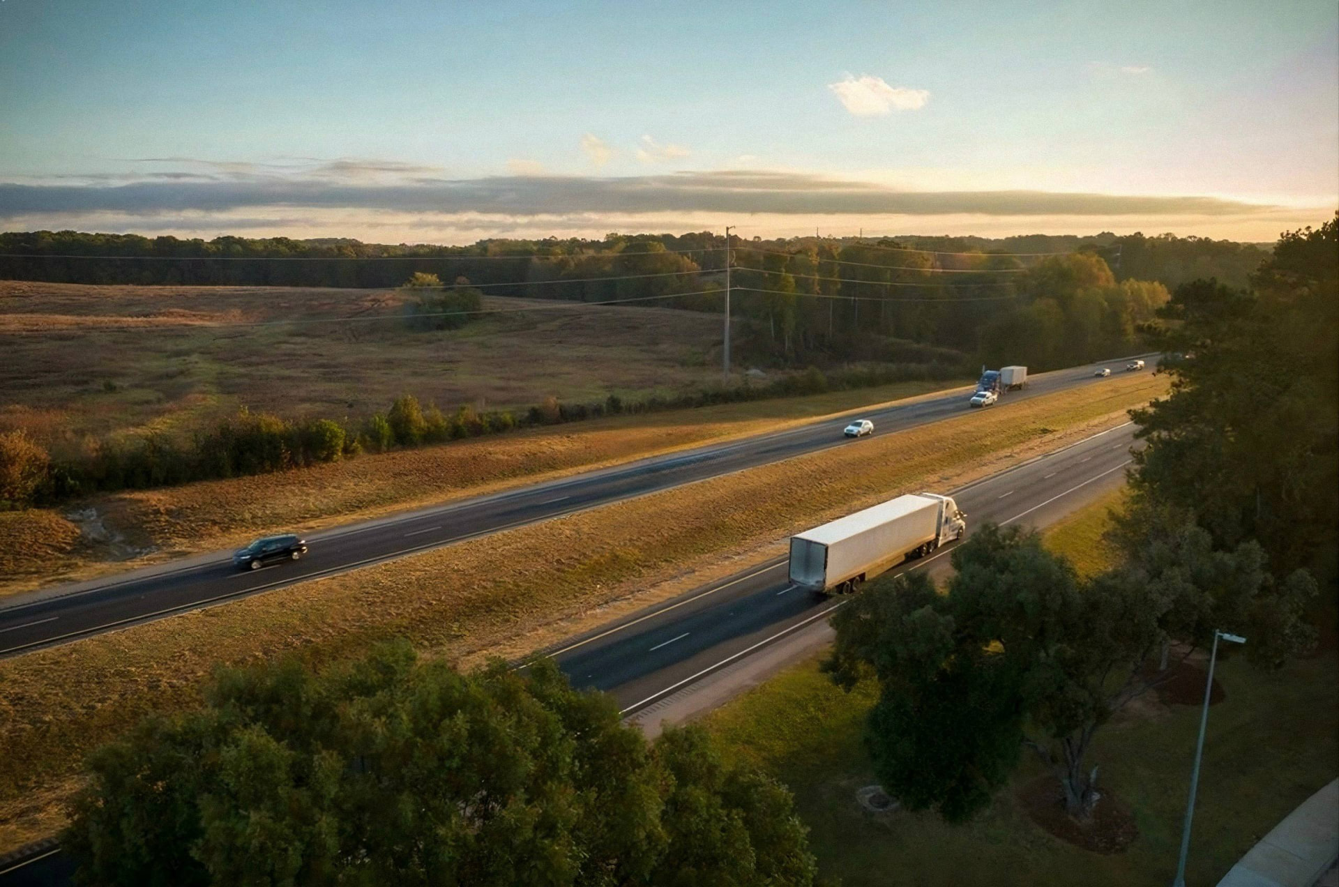 Aerial view of a white dry van tractor-trailer traveling a highway at sunset